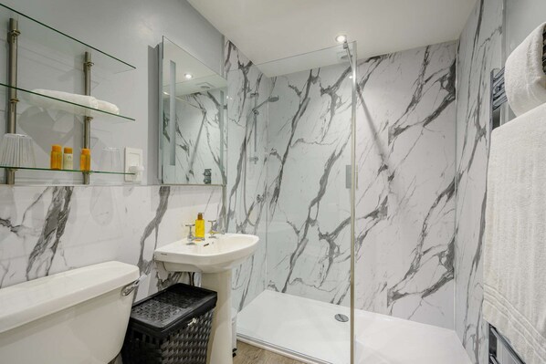 Une salle de bain avec un mur en marbre, une cabine de douche en verre, un lavabo blanc et des toilettes.