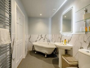 A bathroom with a freestanding bathtub, a sink, and a toilet. There is a mirror above the sink, and a shelf with toiletries.