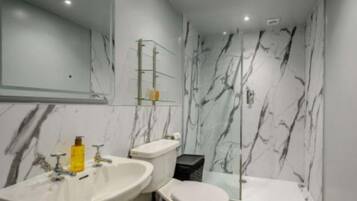 A bathroom with a marble wall, a sink, a toilet, and a bathtub.