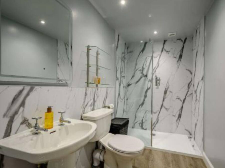 A bathroom with a marble wall, a sink, a toilet, and a bathtub.