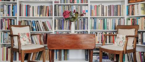 Une pièce comprenant deux chaises en bois, une petite table en bois et une bibliothèque remplie de livres.