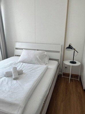 Un lit bien fait, avec du linge de lit blanc et des serviettes pliées, une table de chevet avec une lampe et un plancher en bois.