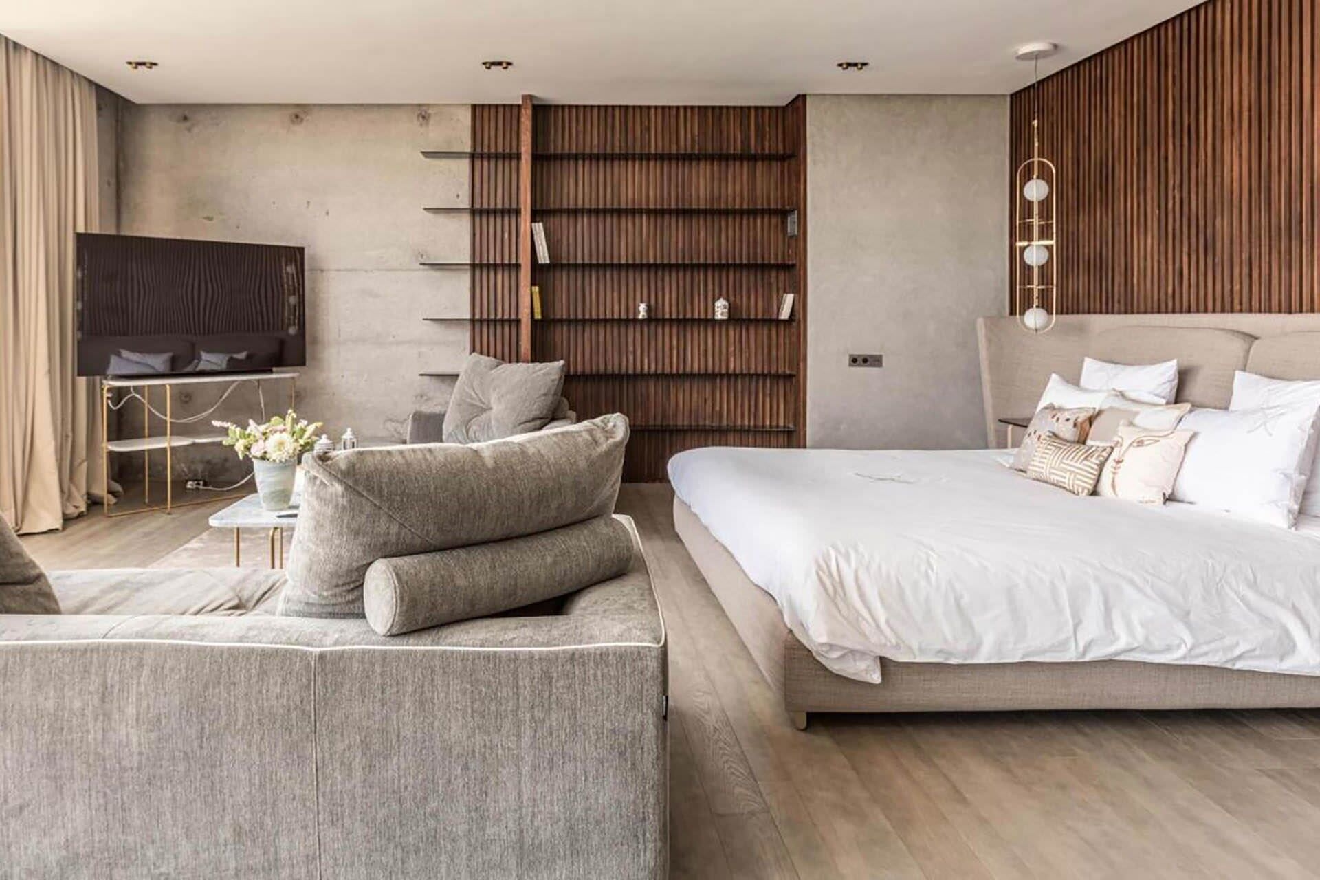 Une chambre à coucher moderne, dotée d’un grand lit, d’un canapé, d’une télévision et d’étagères en bois intégrées.