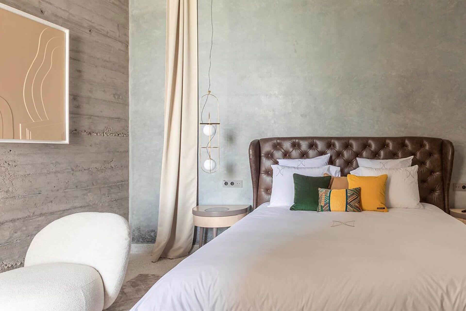 A bedroom with a tufted headboard, a white bedspread, and multiple pillows in various colors.