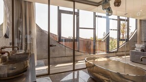 Ein modernes Badezimmer mit einer großen, gläsernen Badewanne, einem Waschtisch mit Goldarmatur und Blick auf eine Holzterrasse.
