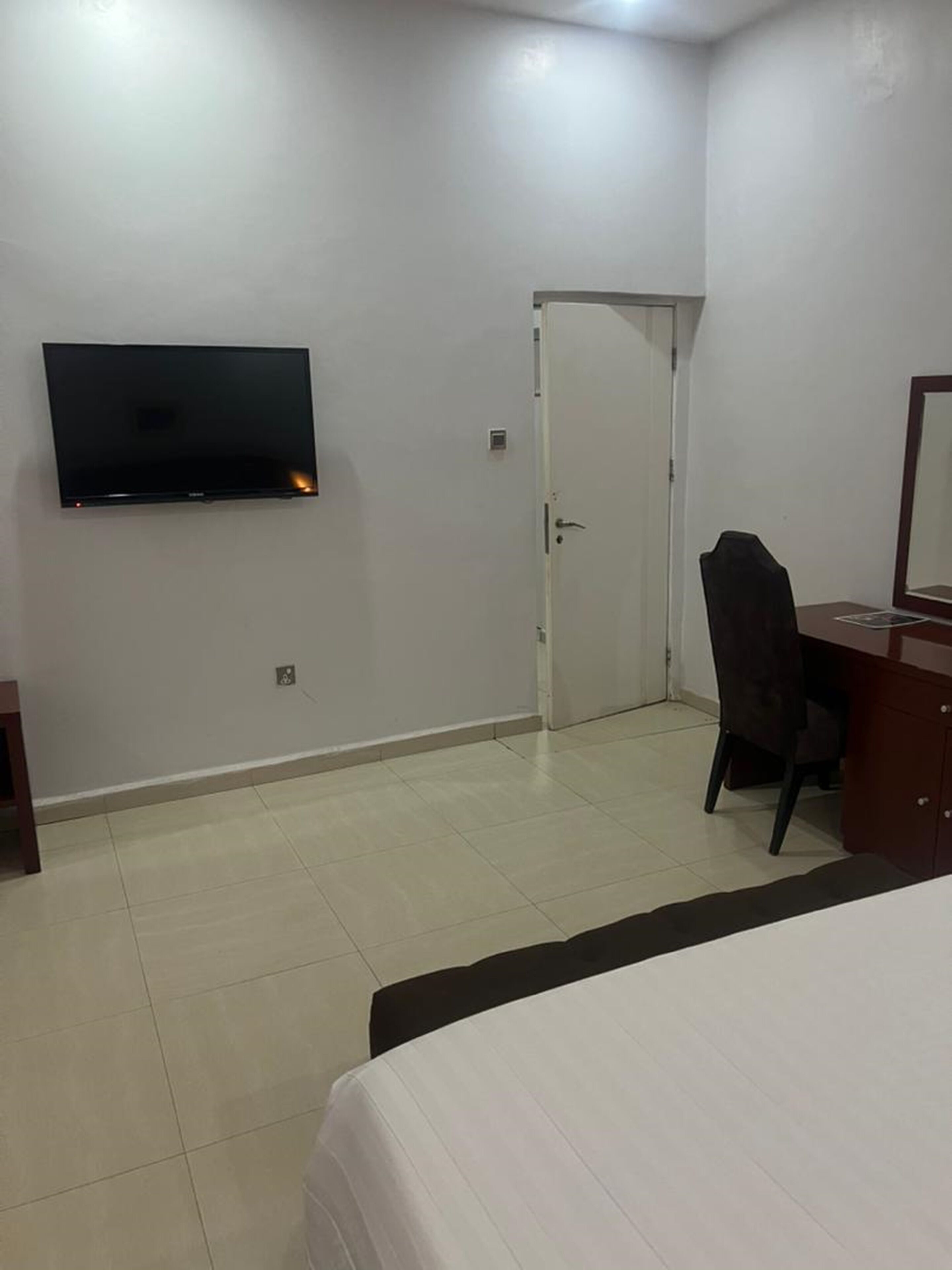 A hotel room with a bed, a desk, a chair, a TV mounted on the wall, and a door.