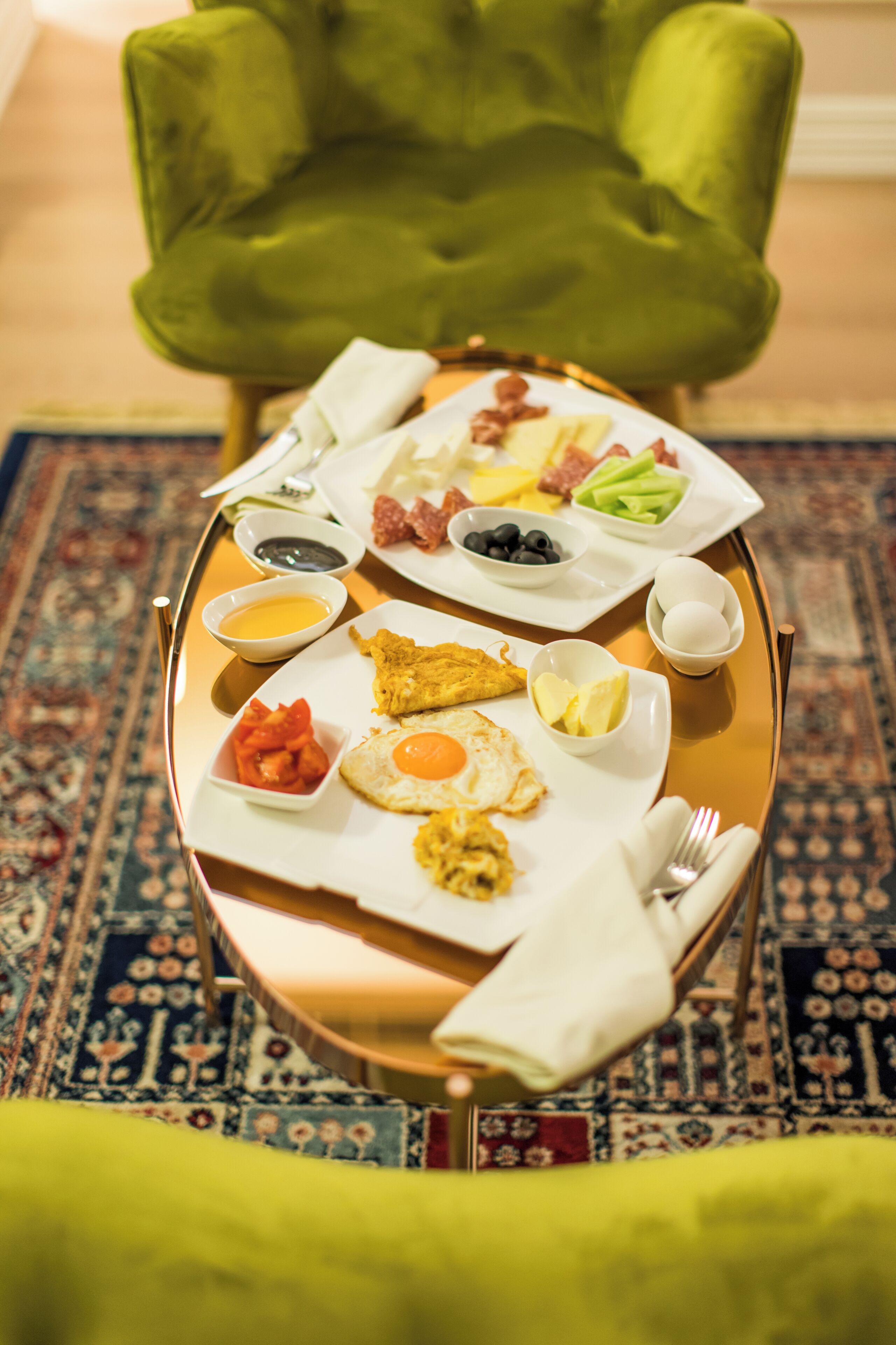 A breakfast tray with eggs, bacon, tomatoes, and various condiments on a patterned rug.