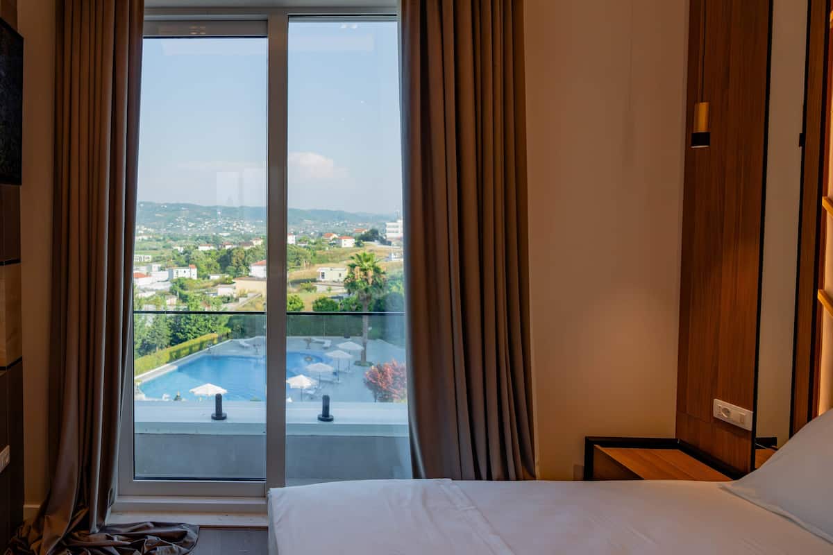 Une chambre d’hôtel avec un lit, une vue sur une piscine et un balcon avec des rideaux.