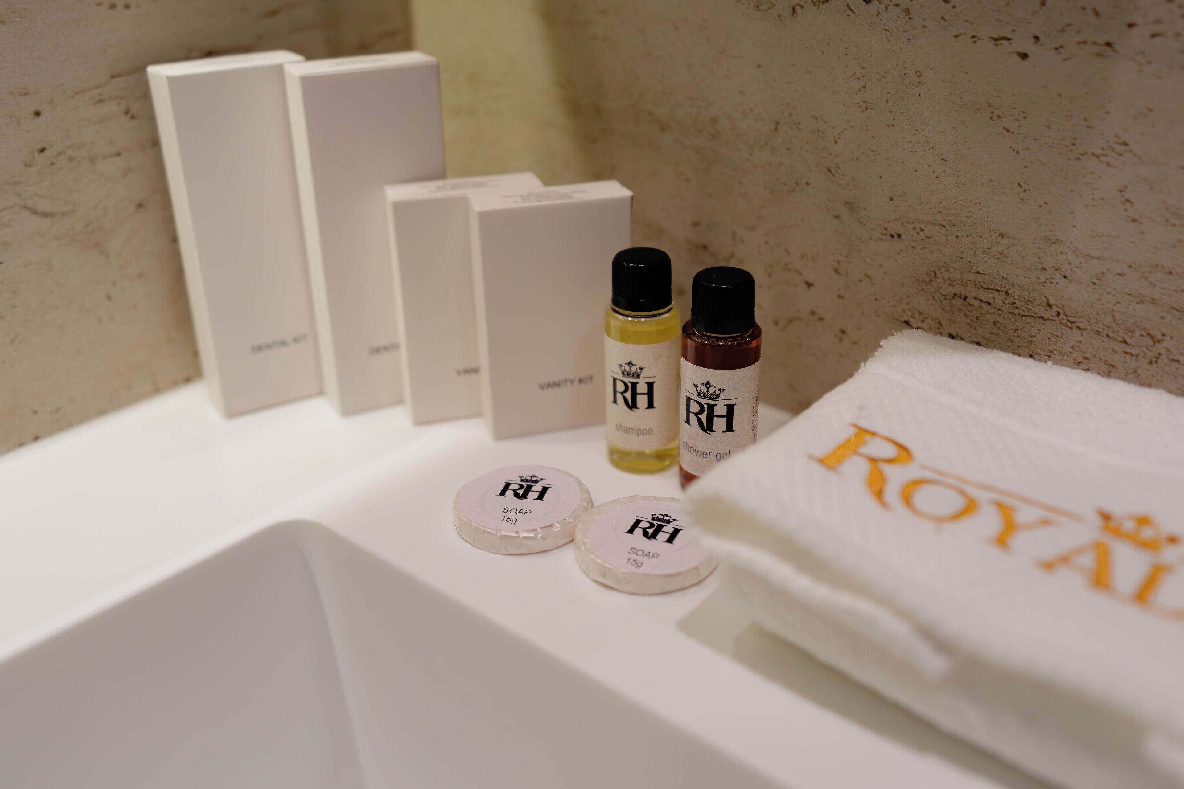 Un baño con un lavamanos blanco, dos dispensadores de jabón, una botella de champú y una toalla con el bordado "ROYAL".