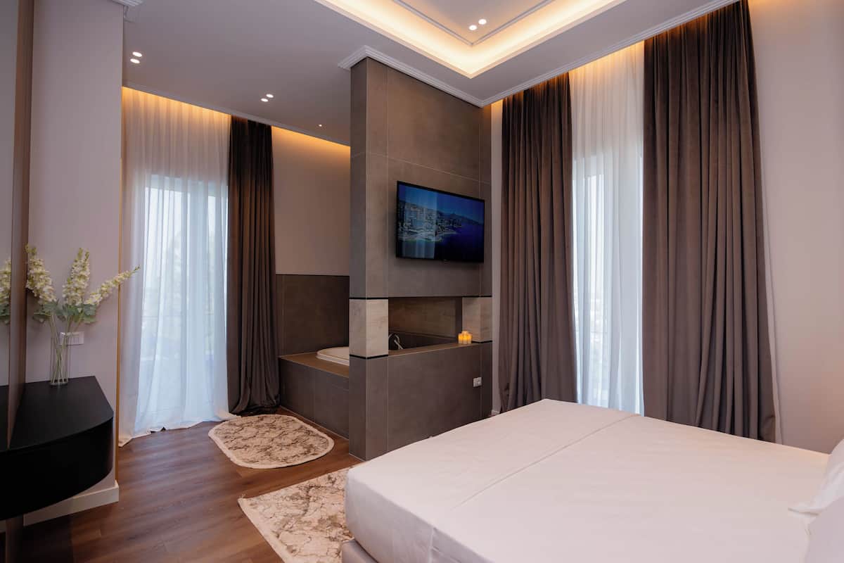 Une chambre d’hôtel moderne dotée d’un grand lit, d’un téléviseur fixé au mur, d’un lavabo intégré et offrant une vue sur la ville par la fenêtre.