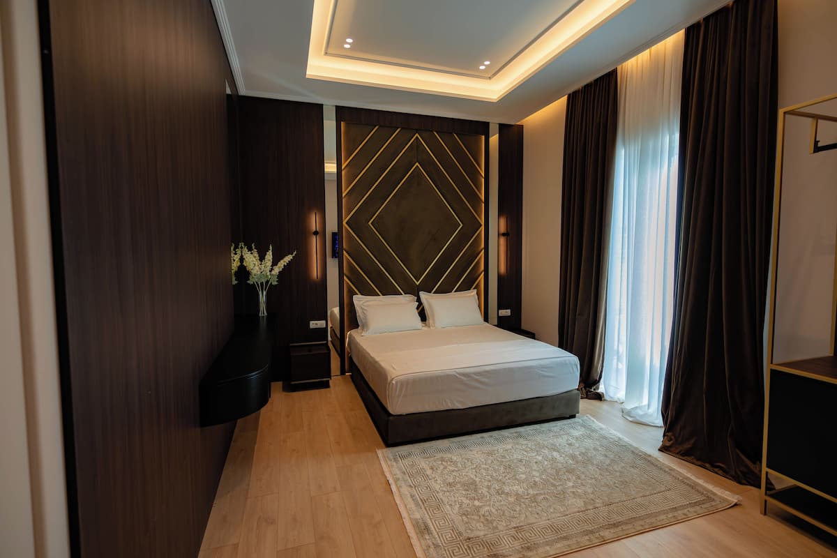 Une chambre moderne avec un grand lit, des lambris en bois foncé, un motif géométrique sur le mur et une grande fenêtre avec des rideaux.