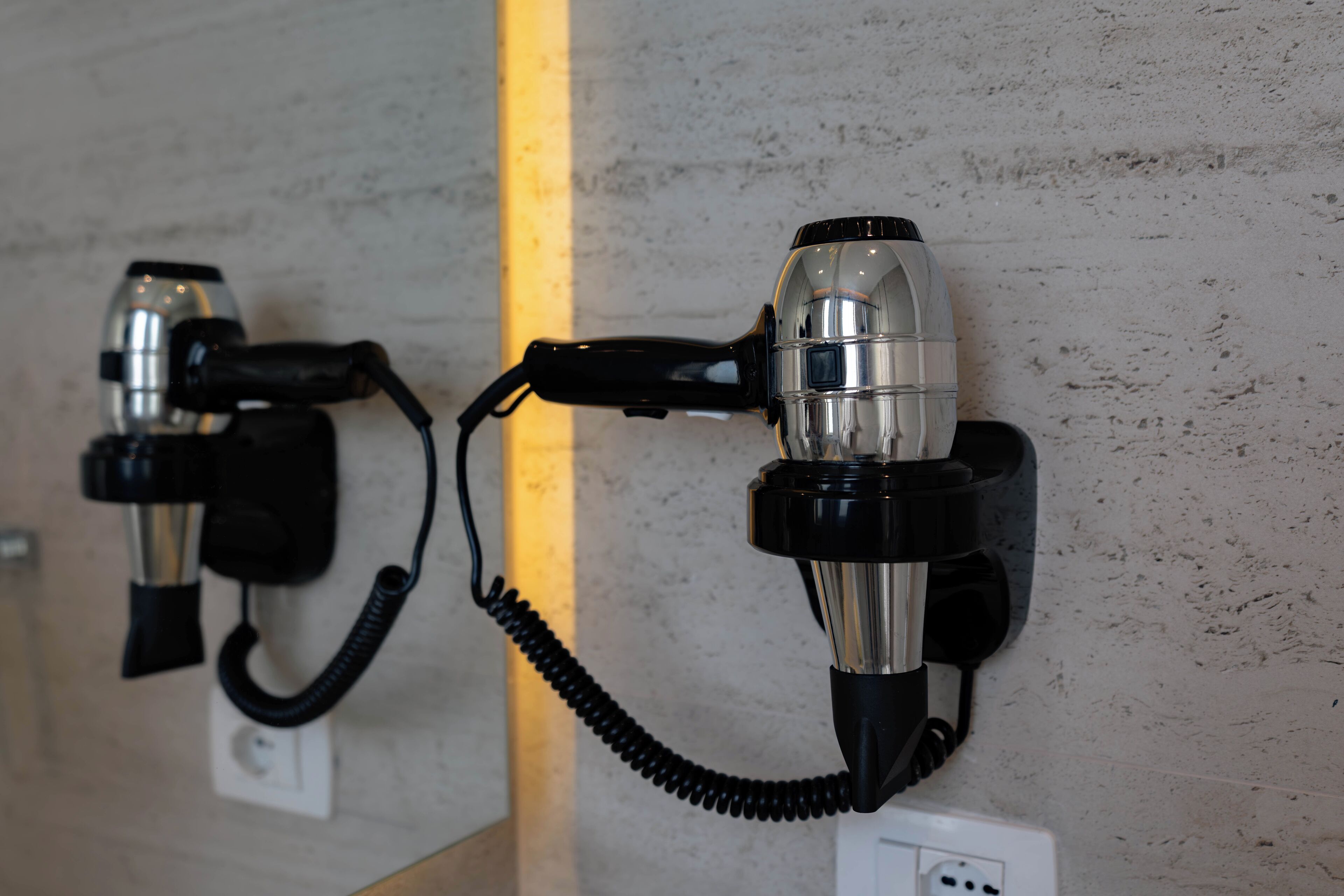 Two hair dryers mounted on a textured wall, connected by a coiled cord.