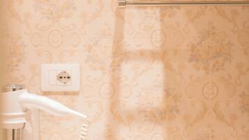 A bathroom with a patterned wallpaper, a towel rack with folded towels, and a hairdryer plugged into a wall socket.