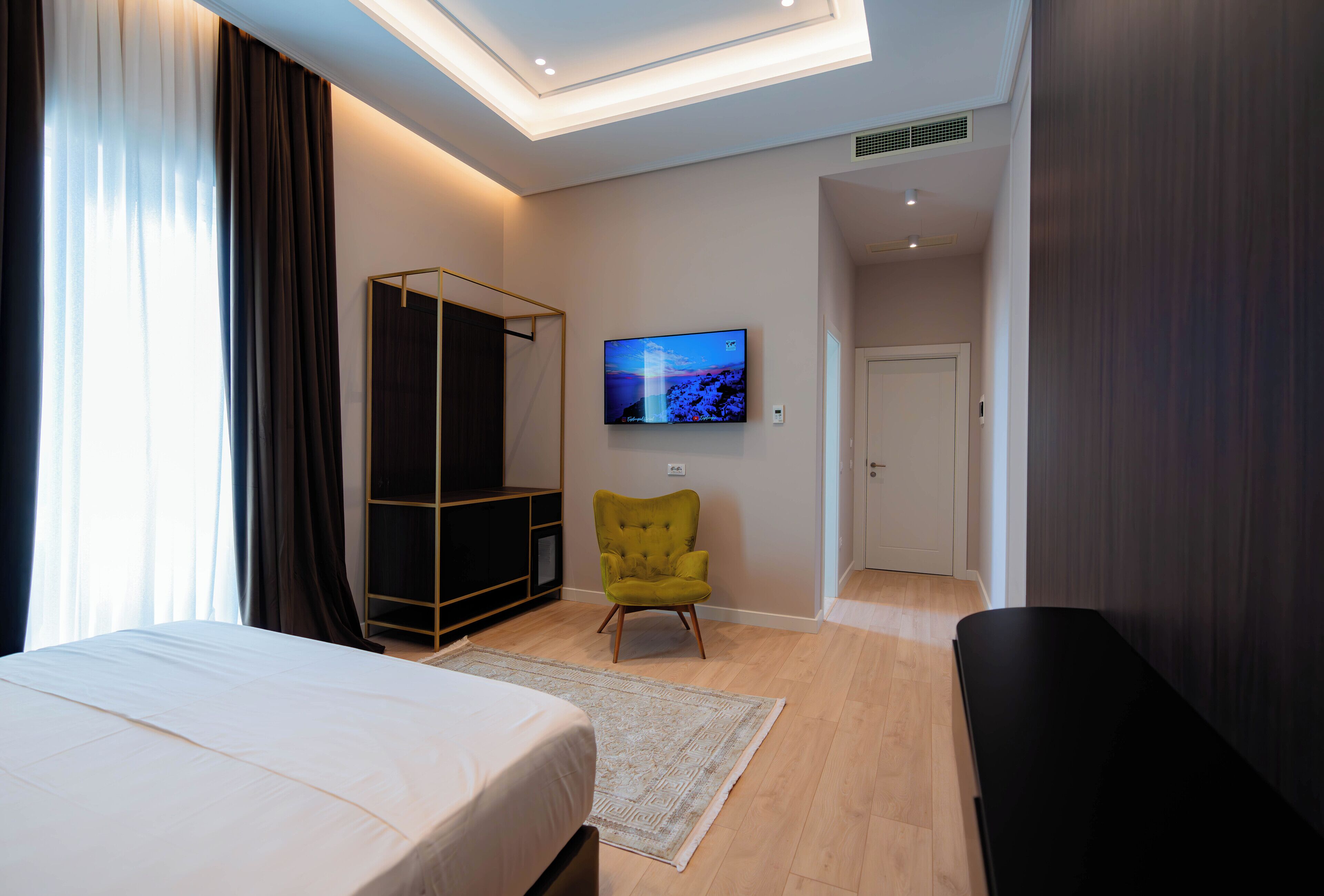A modern hotel room with a bed, a green armchair, a TV, and a walk-in closet.