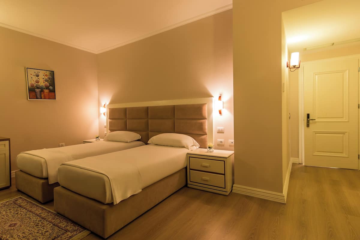 Une chambre d’hôtel avec deux lits, un bureau, une chaise, une petite table et un tableau au mur.