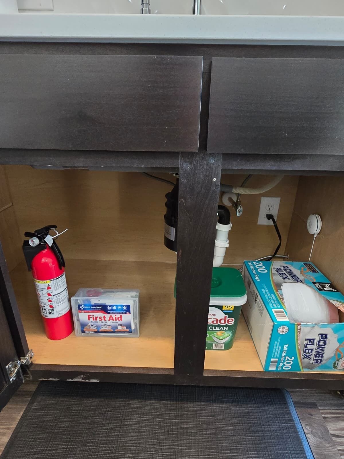 A kitchen area with a fire extinguisher, first aid kit, cleaning supplies, and a power outlet.