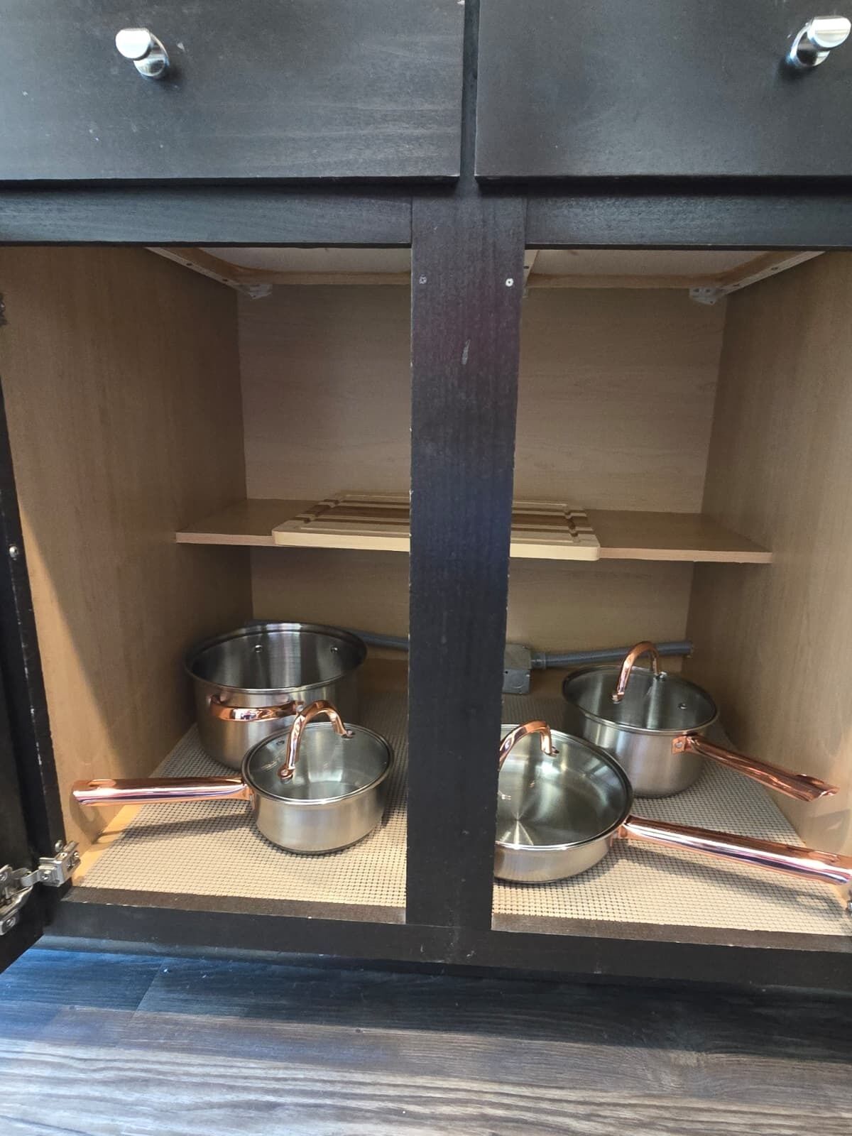 Un meuble de cuisine contenant des casseroles et des poêles en métal, rangées sur des étagères métalliques.