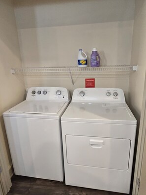 Ein Waschraum mit zwei weißen Whirlpool-Waschmaschinen und einem darüberliegenden Regal mit Reinigungsmitteln.