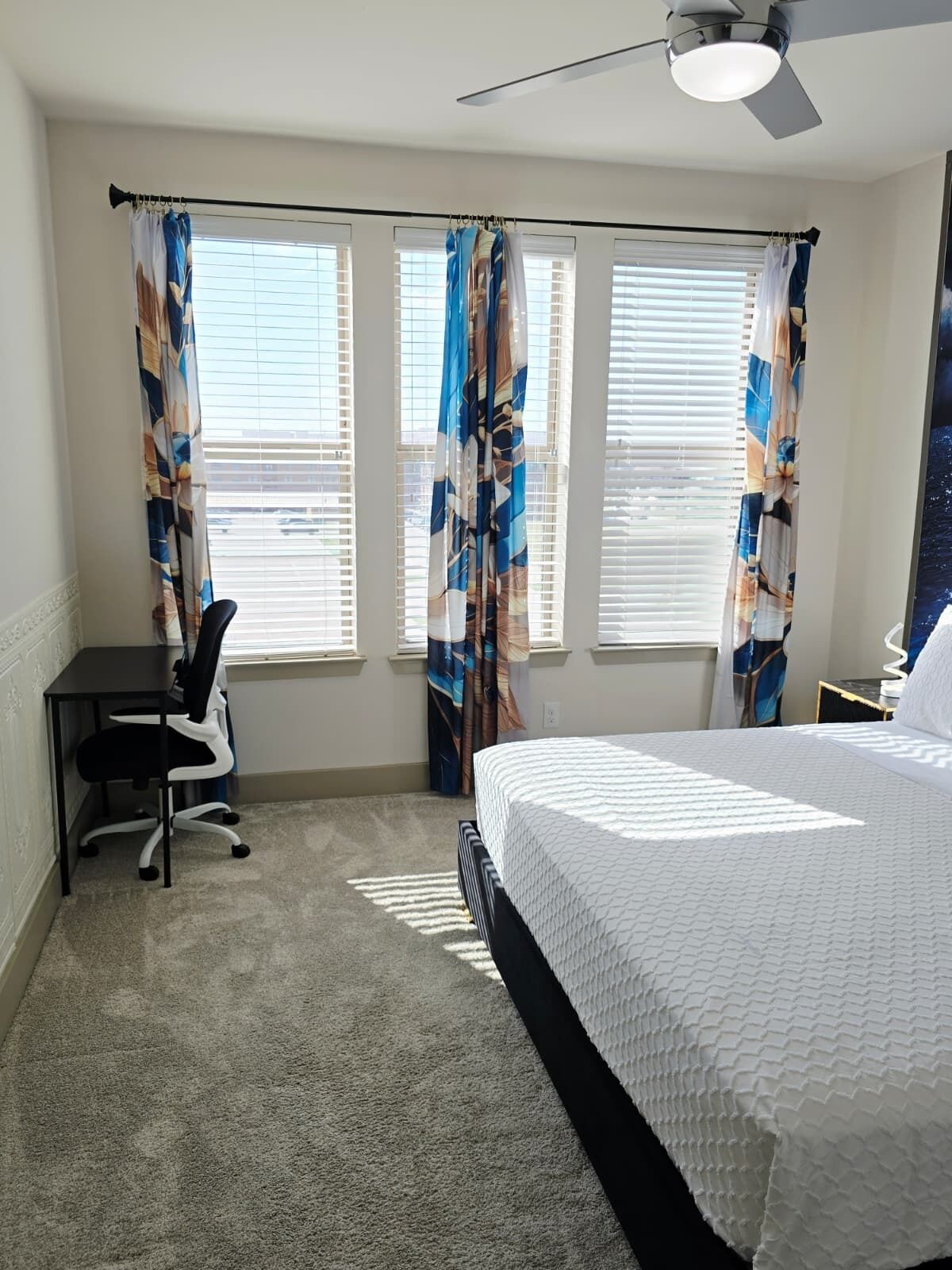 A bedroom with a bed, a desk, and two windows with curtains.