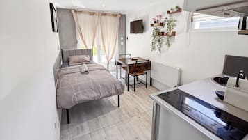 A compact bedroom with a bed, a desk, and a kitchenette.