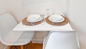 A modern dining area with a flat-screen TV mounted above a white table set for two. - Au42BisJM (Cambrai)