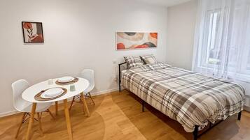 Un dormitorio con una cama, una mesa de comedor con sillas y dos obras de arte en las paredes.