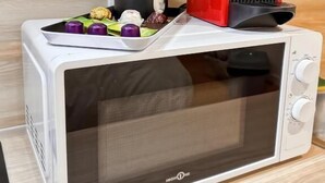 A microwave oven with a red coffee maker on top, a tray with various food items, and a black container. - Au42BisJM (Cambrai)