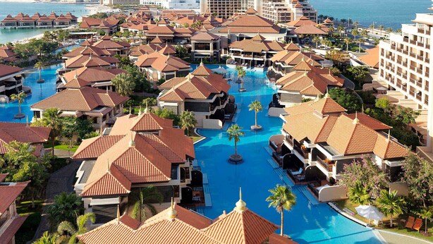Un resort con varias piscinas, palmeras y vistas a la playa.