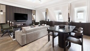 En moderne stue med et stort fladskærms-tv, mørk træpanelfacade, en modulsofa og et spiseområde med et marmorbord.