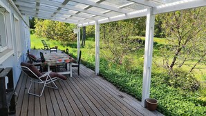 Une terrasse extérieure couverte, dotée d’une table et de chaises, et entourée d’une végétation luxuriante.
