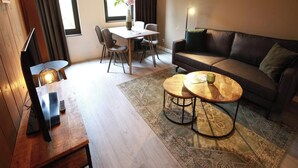 Una sala de estar moderna con un sofá, dos mesas auxiliares, una mesa de comedor con sillas, un televisor y una lámpara.