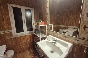 A bathroom with a white sink, a toilet, a window, and a mirror.