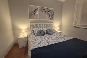 A bedroom with a bed, two bedside tables, a wall-mounted artwork, and a window with a curtain.