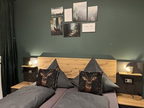 A bedroom with a wooden headboard, two bedside tables with lamps, a bed with grey bedding, and four framed pictures on the wall. - 100 sqm cozy apartment with fireplace – quiet and modern – Stay TNT (Geislingen)