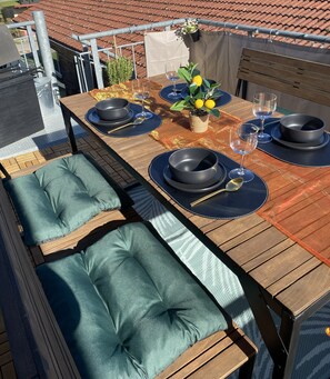 A wooden dining table with blue placemats, black bowls, and wine glasses, set on a terrace with a view of a tiled roof. - 100 sqm cozy apartment with fireplace – quiet and modern – Stay TNT (Geislingen)