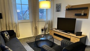 Una sala de estar moderna con un sofá, sillones, una mesa de centro y un televisor sobre un soporte de madera.