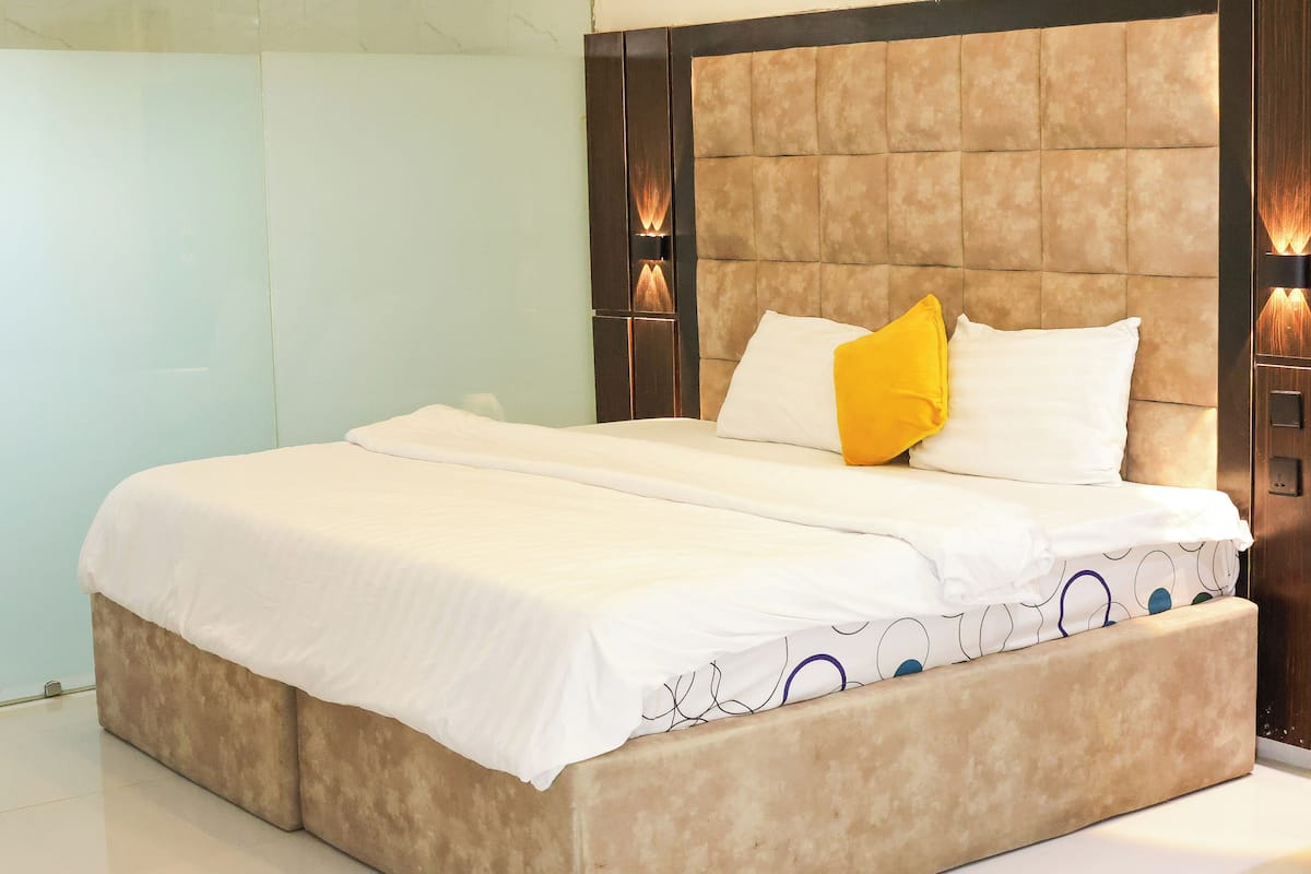 Una cama con cabecera color beige, ropa de cama blanca y una sola almohada amarilla.