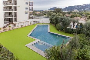 A swimming pool surrounded by a green lawn, with a multi-story building in the background. - Charming T1 in residence with view on swimming pool (Porto-Vecchio)