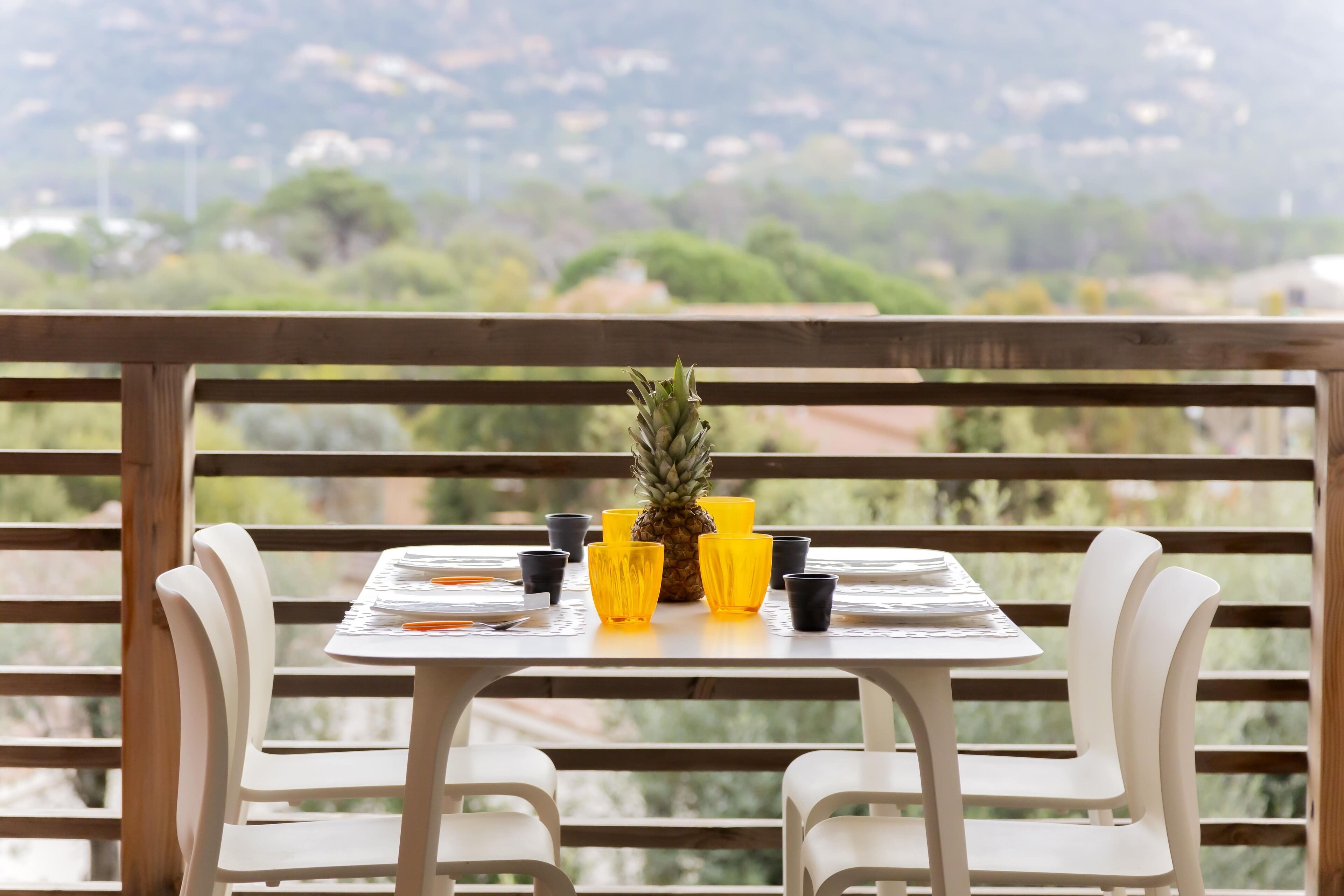 Une table dressée avec des verres jaunes, un ananas et une chaise blanche.