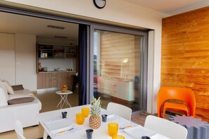 A modern living room with a sofa, a dining table with yellow cups and a pineapple, and a kitchen in the background. - Charming T1 in residence with view on swimming pool (Porto-Vecchio)