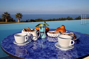 A round table with a blue marble top, set with white cups, a blue teapot, and a plate of pastries and fruits. - Villa CYN-pool, billiards, piano and miniature golf (Santo Stefano di Camastra)