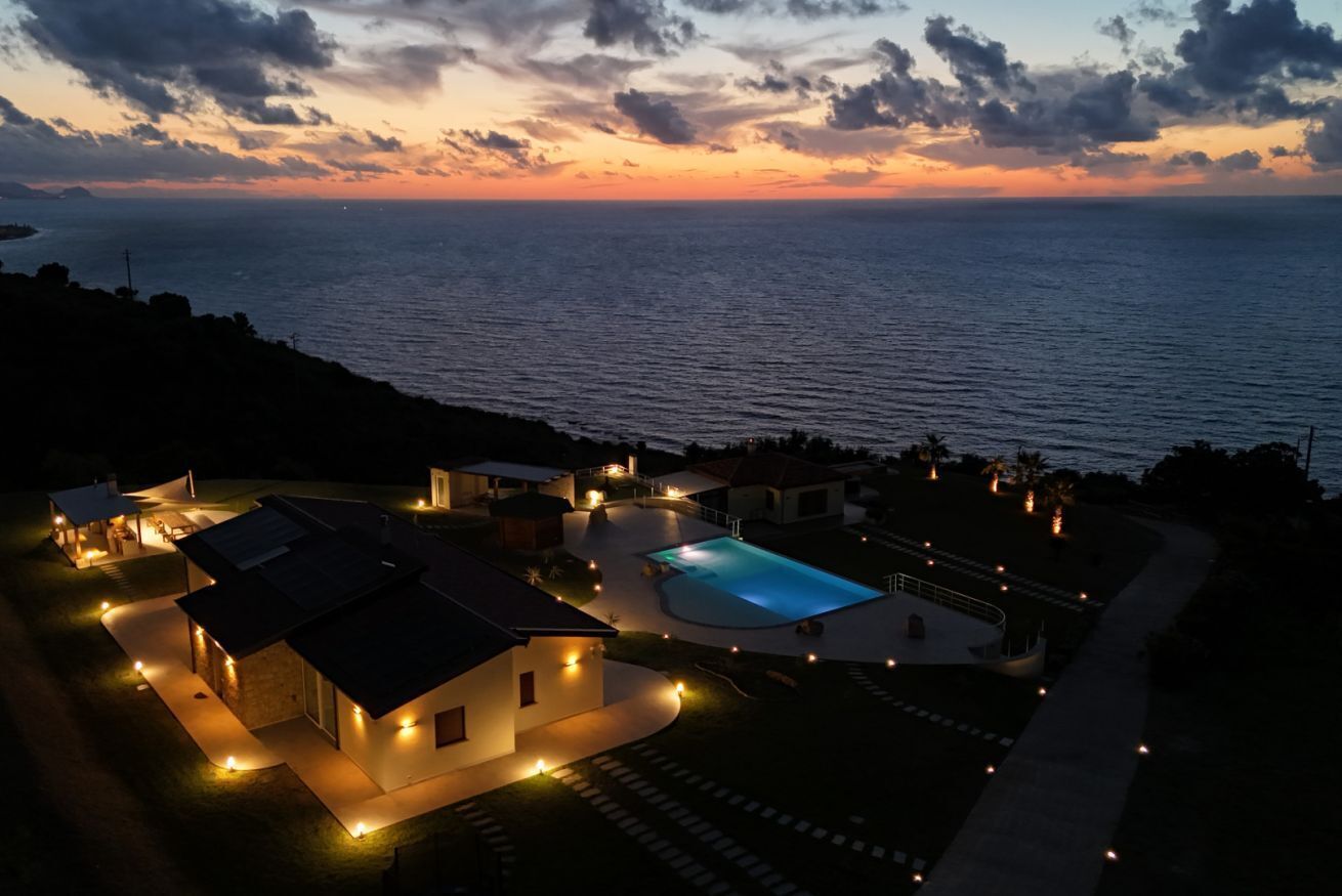 A residential property with a swimming pool, multiple houses, and a view of the sea at dusk.