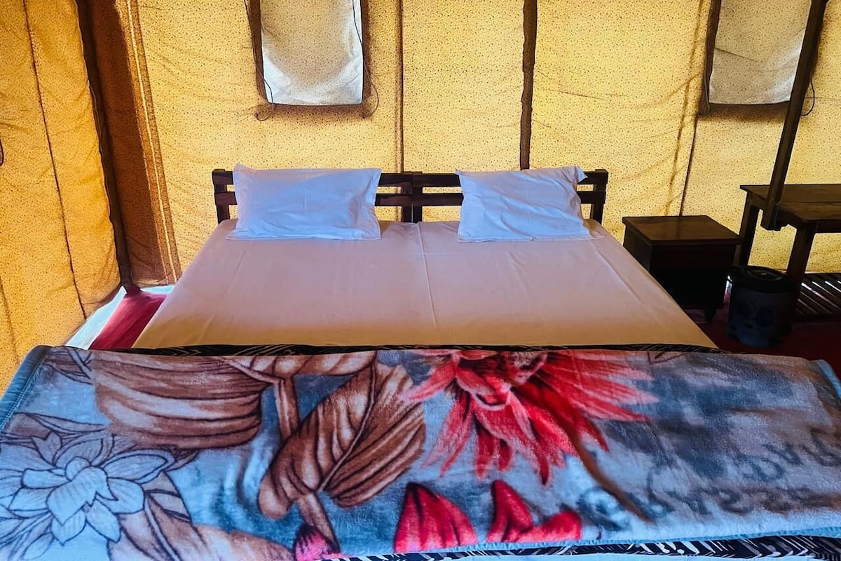 Un lit avec une couvre-lit à motifs floraux, deux oreillers et une tête de lit en bois. Deux petites tables avec des lampes se trouvent de chaque côté du lit.