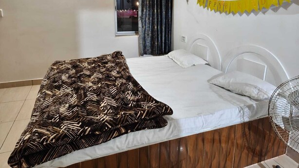 A bedroom with a bed, a window with curtains, a fan, and a yellow 'HAPPY BIRTHDAY' banner. - Shree Karni Hotel & Restaurant (Bikaner)
