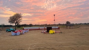 An outdoor event setup with a stage, chairs, and a vehicle in a sandy area. - Shree Karni Hotel & Restaurant (Bikaner)