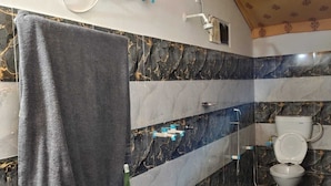 A bathroom with a marble backsplash, a towel hanging on the wall, a toilet, and a hand dryer. - Shree Karni Hotel & Restaurant (Bikaner)