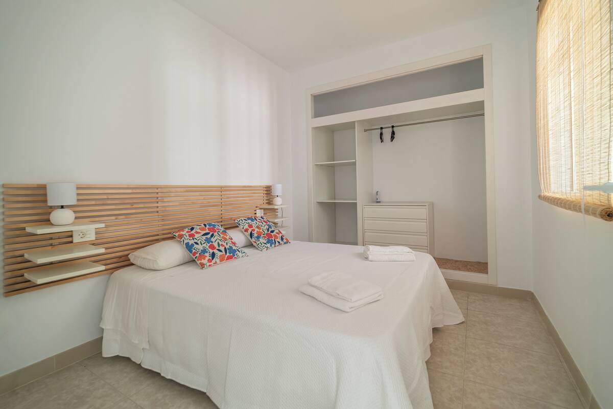 A bedroom with a bed, bedside lamps, a wardrobe, and a window with a wicker blind.