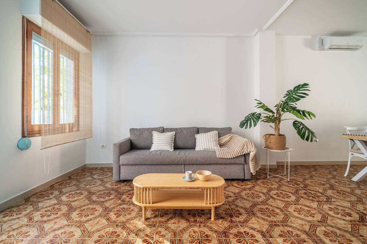 A living room with a grey sofa, a wooden coffee table, a potted plant, and patterned flooring.