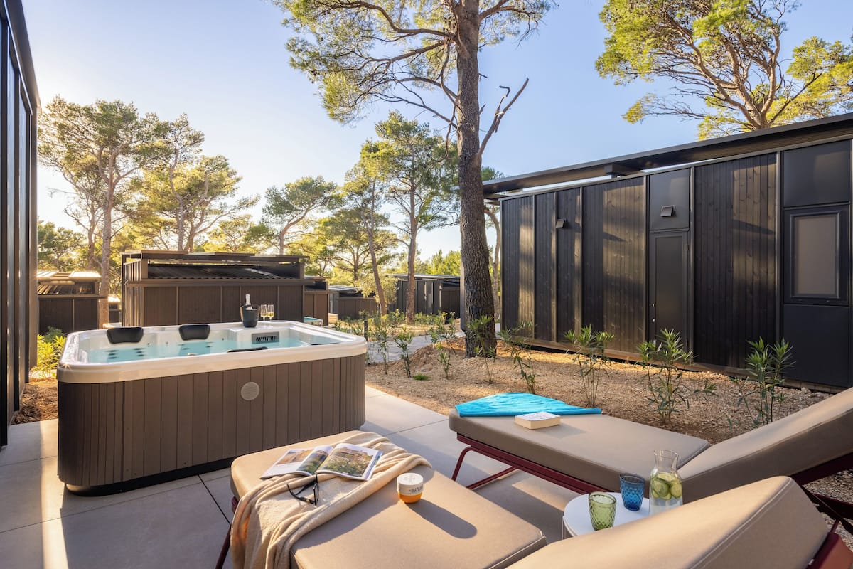 A hot tub, lounge chairs, and a small table with drinks and a book in a backyard setting.