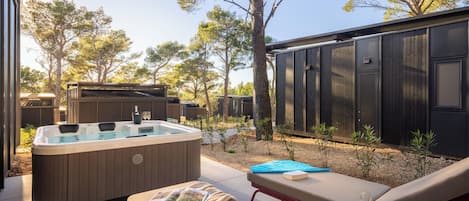 A hot tub, lounge chairs, and a small table with drinks and a book in a backyard setting.